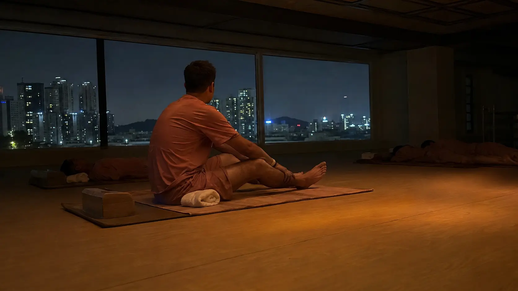Foreign visitor resting on a mat in the communal sleeping room of a Korean sauna complex at night