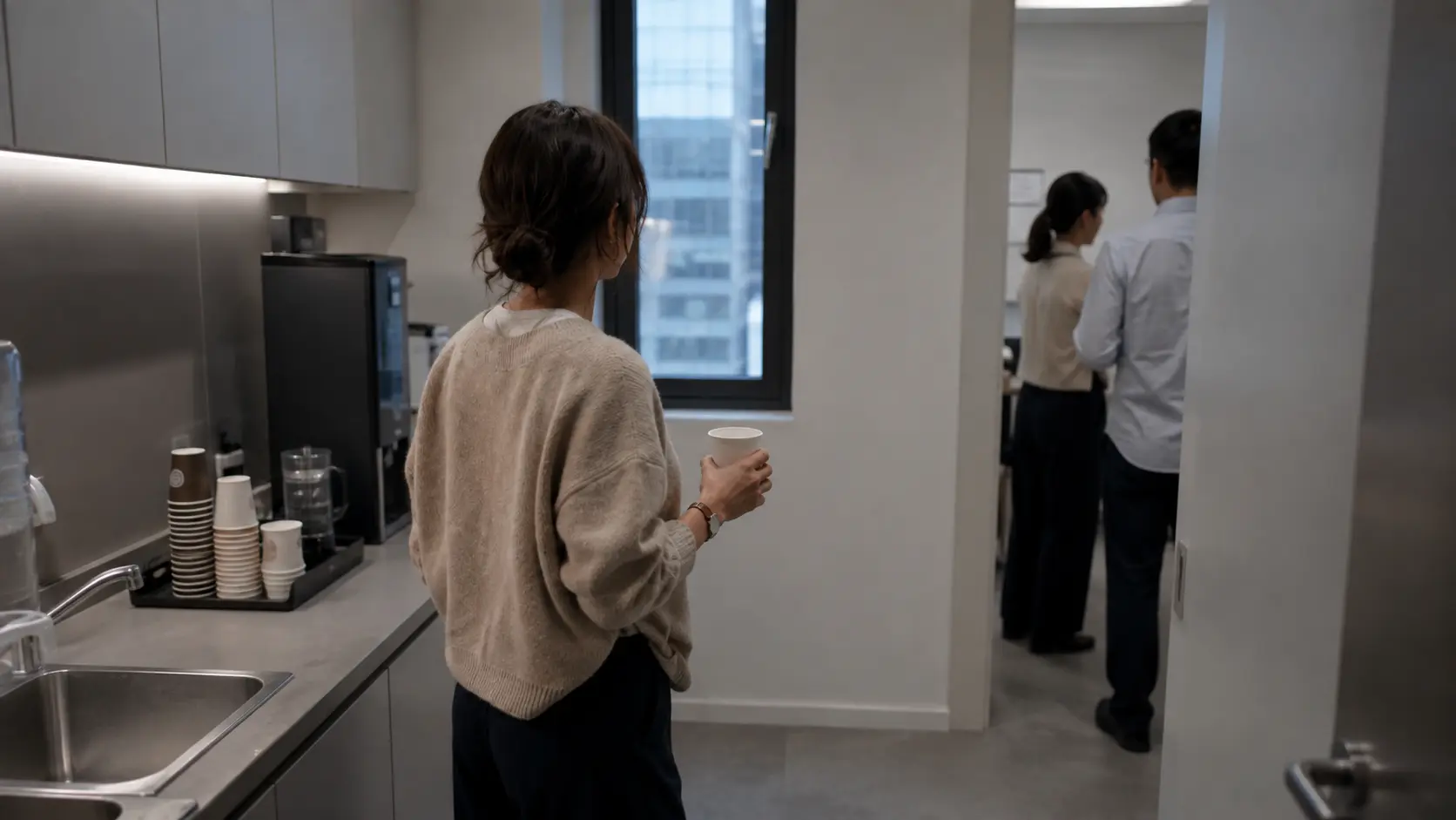 Foreign employee in beige cardigan typing a Korean workplace message at an office desk in the evening